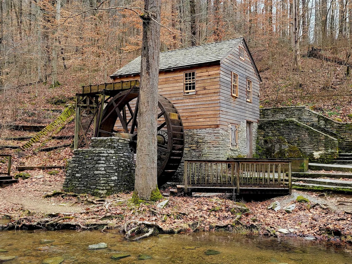 Wooden gristmill and waterwheel beside a wooded creek
